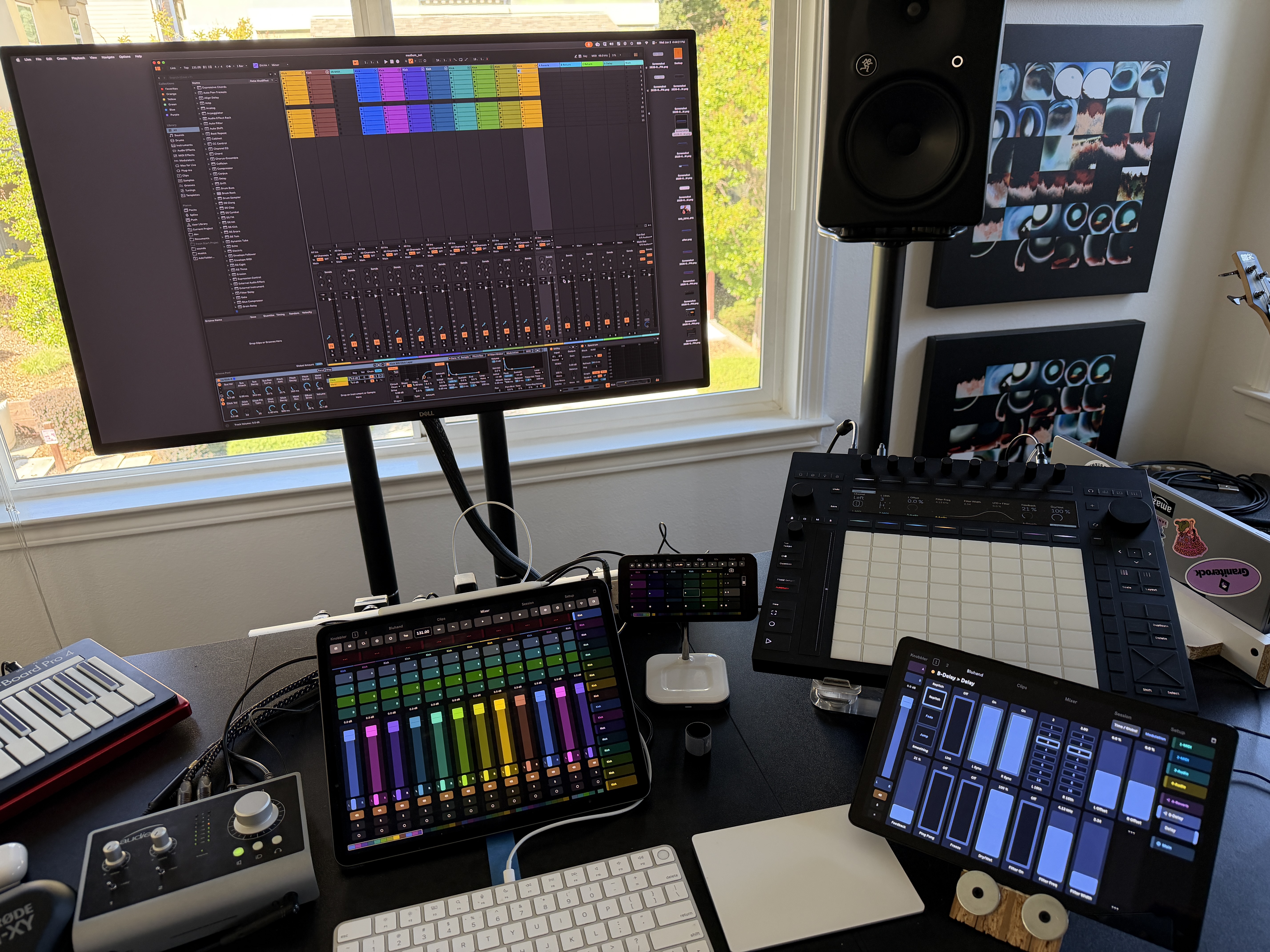 A studio desk: a monitor running Ableton Live with a multi-track mixer and meters, a Push controller, a phone, and two tablets each running Knobbler — one showing the multi-track mixer, the other the session clip grid